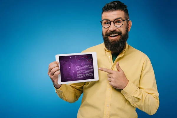 Fröhlicher bärtiger Mann zeigt auf digitales Tablet mit Infografik, isoliert auf blauem Grund — Stockfoto