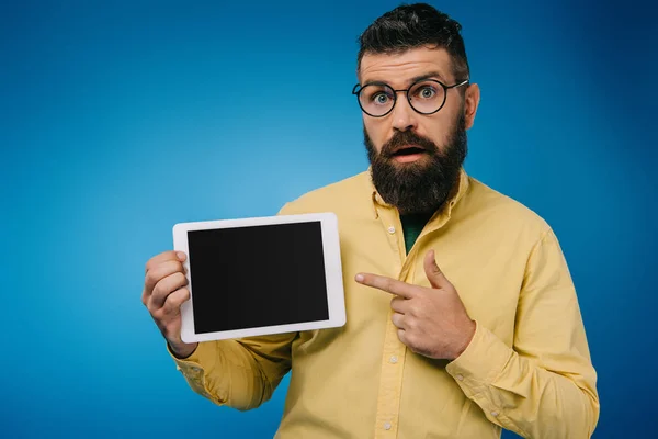 Uomo barbuto interessato che punta al tablet digitale con schermo bianco, isolato su blu — Foto stock