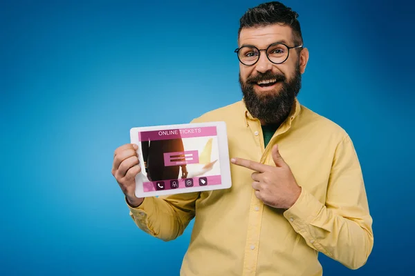 Happy bearded man pointing at digital tablet with online tickets app, isolated on blue — Stock Photo