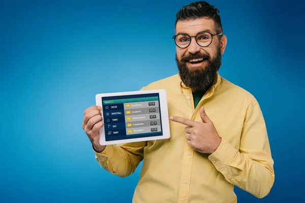 Heureux homme barbu pointant vers tablette numérique avec application de sport, isolé sur bleu — Photo de stock