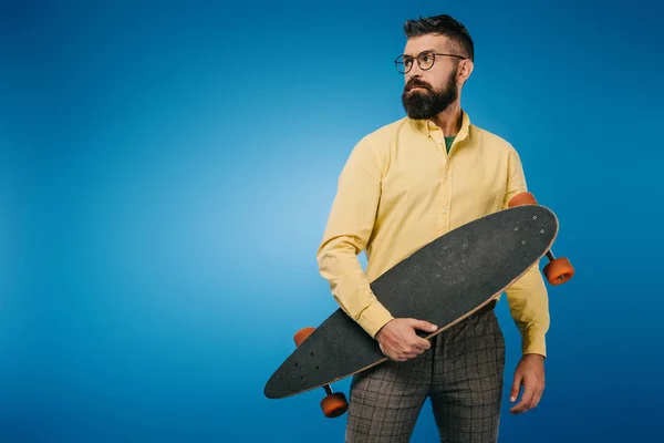 Schöner bärtiger Mann hält Longboard isoliert auf blauem Grund — Stockfoto