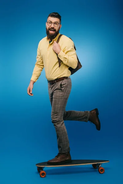 Збуджений бородатий чоловік скейтбординг в студії на синьому — стокове фото