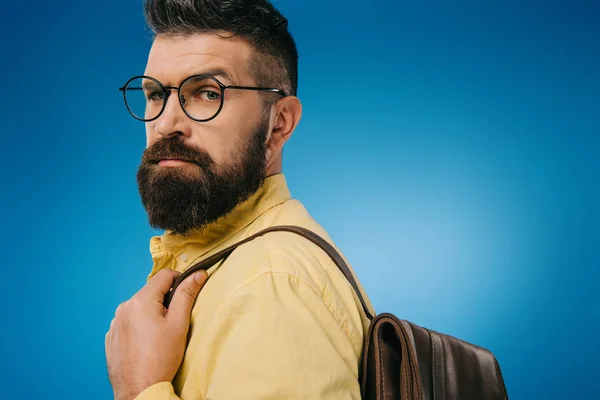 Ernster bärtiger Mann mit Brille und Rucksack, isoliert auf blauem Grund — Stockfoto
