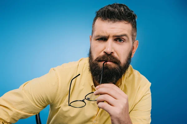 Подозрительный бородатый мужчина в очках, изолированных на синий — стоковое фото