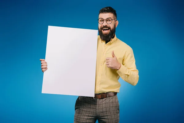 Happy bearded man showing thumb up and holding empty board isolated on blue — Stock Photo