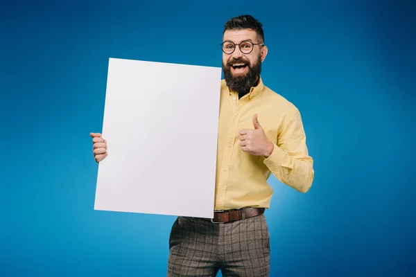 Glücklicher bärtiger Mann zeigt Daumen hoch und hält leeres Brett isoliert auf blauem Grund — Stockfoto