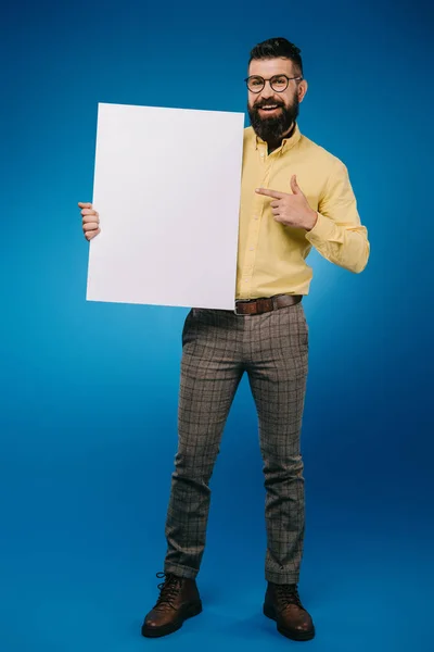 Homme souriant barbu pointant vers la plaque vide isolé sur bleu — Photo de stock