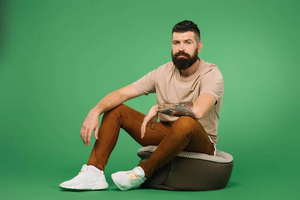 Handsome tattooed bearded man sitting on green — Stock Photo