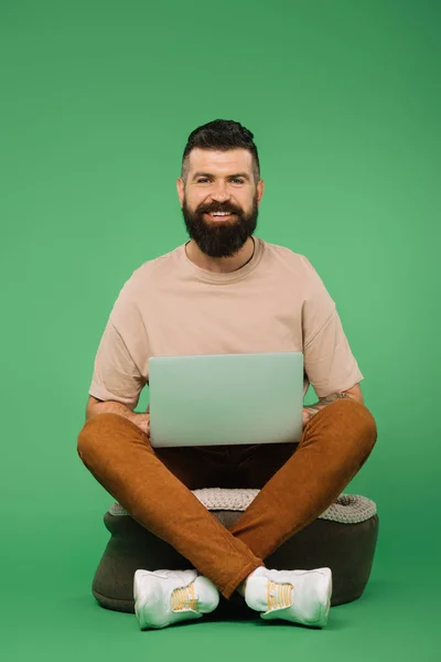 Усміхнений бородатий чоловік використовує ноутбук ізольований на зеленому — стокове фото