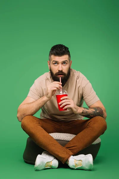 Interested handsome bearded man drinking soda on green — Stock Photo