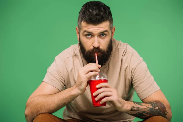 Заинтересованный бородатый мужчина пьет содовую, изолированную от зелени — стоковое фото