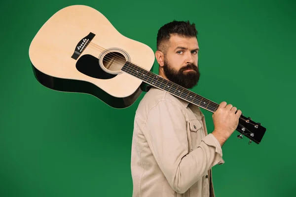 Guitarrista masculino barbudo sosteniendo la guitarra acústica, aislado en verde - foto de stock