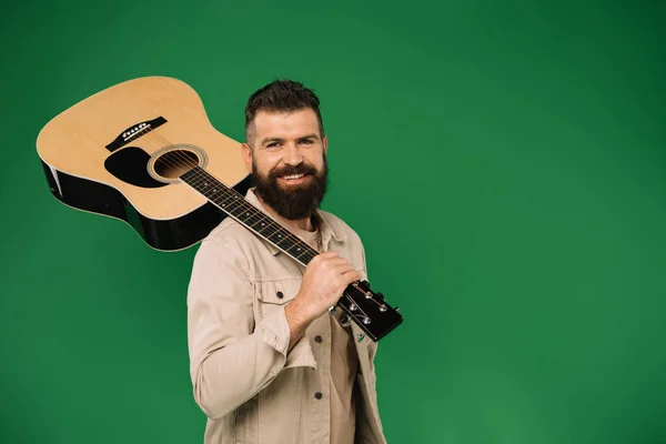 Guapo sonriente hombre sosteniendo la guitarra acústica, aislado en verde - foto de stock