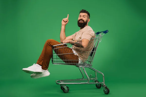 Souriant homme pointant vers le haut et assis dans le panier isolé sur vert — Photo de stock