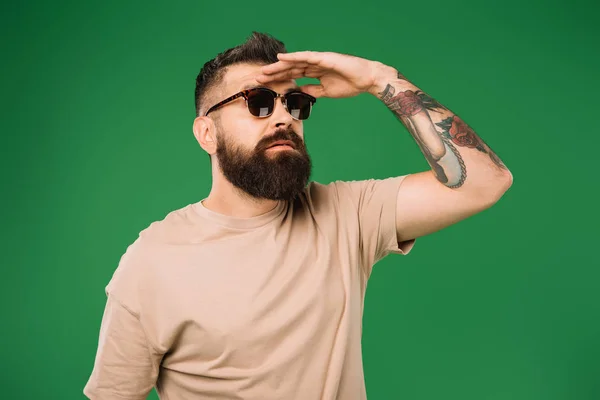Hombre tatuado en gafas de sol mirando hacia otro lado, aislado en verde - foto de stock