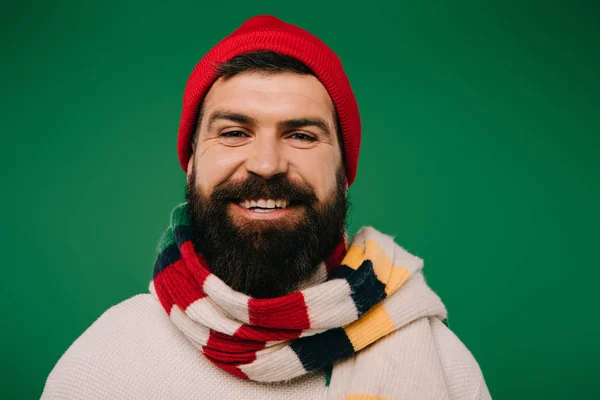 Homme barbu souriant dans le chapeau et l'écharpe isolé sur vert — Photo de stock