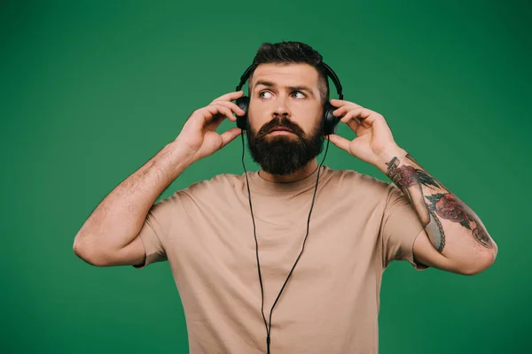 Handsome tattooed man listening music in headphones isolated on green — Stock Photo