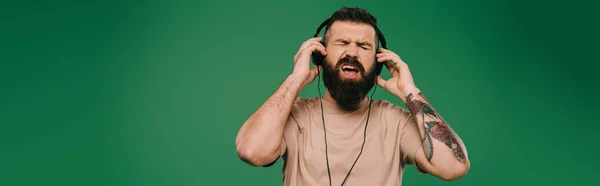 Tattooed man singing listening music in headphones isolated on green — Stock Photo