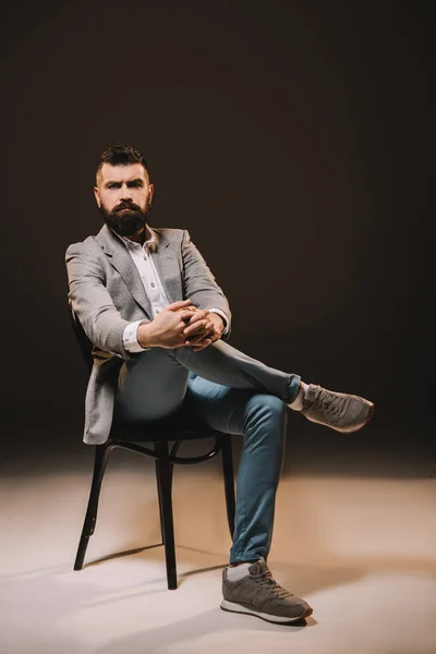 Красива борода бізнесмен в сірому піджаку сидить на стільці ізольовано на коричневому — стокове фото