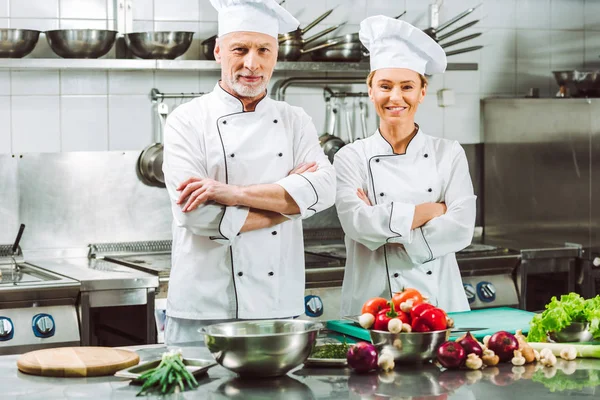 Chef di sesso femminile e maschile in uniforme con le braccia incrociate durante la cottura in cucina ristorante — Stock Photo