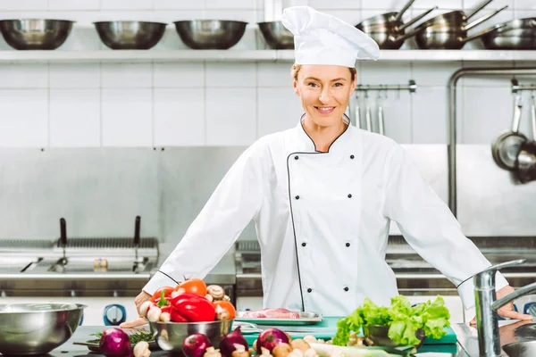 Bela chef feminino em uniforme sorrindo e olhando para a câmera durante a cozinha do restaurante — Fotografia de Stock