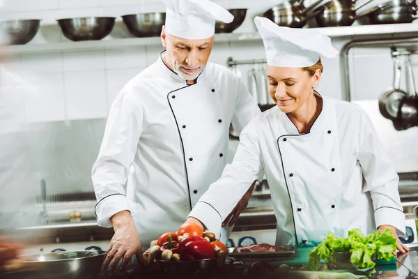 Selektiver Fokus weiblicher und männlicher Köche in Uniform und Hüten beim Kochen in der Restaurantküche — Stockfoto