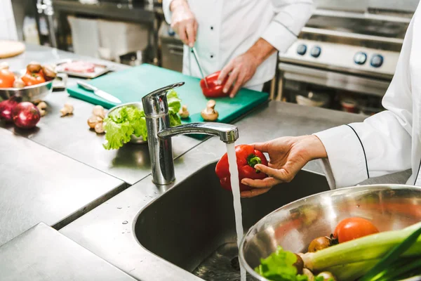 Cropped view of female chef washing pepper in restaurant kitchen — Stock Photo
