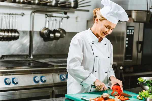 Belle chef féminine en uniforme couper le poivre dans la cuisine du restaurant — Photo de stock