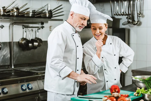 Жіночі та чоловічі кухарі в уніформі розмовляють під час приготування їжі на кухні ресторану — стокове фото