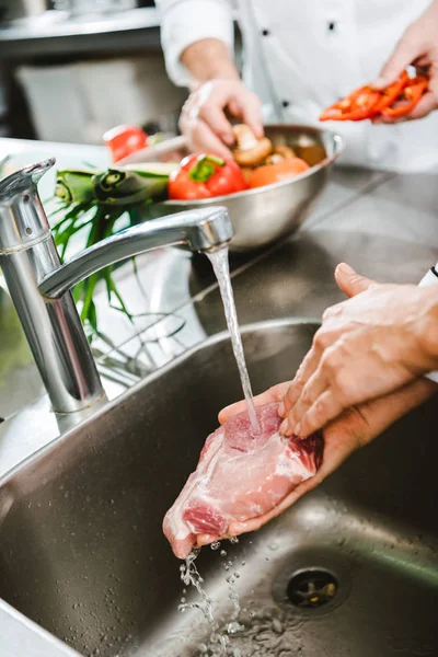 Vista recortada de la cocinera lavando carne cruda en la cocina del restaurante - foto de stock