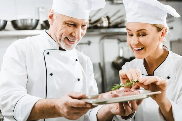 Chef masculino feliz presentación de plato de carne a colega en la cocina del restaurante - foto de stock