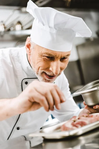 Chef masculino en plato de condimento uniforme en la cocina del restaurante - foto de stock