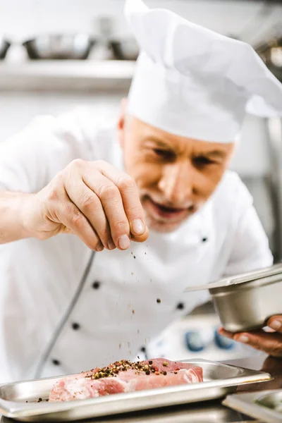 Male chef in uniform seasoning meat in restaurant kitchen — Stock Photo