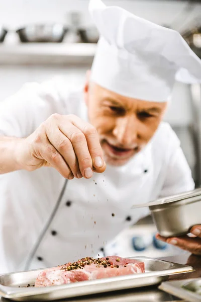 Chef masculino en uniforme condimento carne en la cocina del restaurante - foto de stock