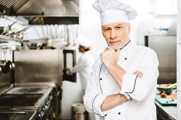 Handsome male chef propping chin with hand and looking at camera in restaurant kitchen — Stock Photo