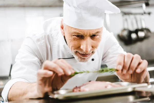 Male chef in uniform decorating dish with herb in restaurant kitchen — Stock Photo