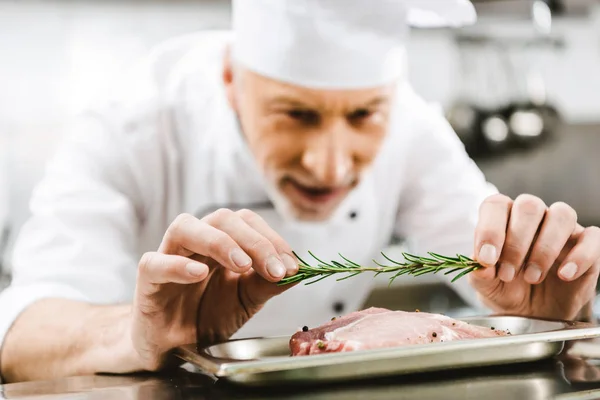 Chef masculino en uniforme decorando plato de carne con hierba de romero en la cocina del restaurante - foto de stock