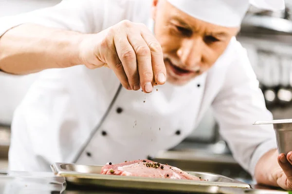 Chef masculino en uniforme condimento carne en la cocina del restaurante - foto de stock