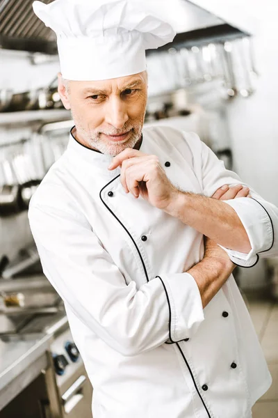 Selektiver Fokus eines gutaussehenden, nachdenklichen männlichen Kochs, der in der Restaurantküche sein Kinn mit der Hand stützt — Stockfoto