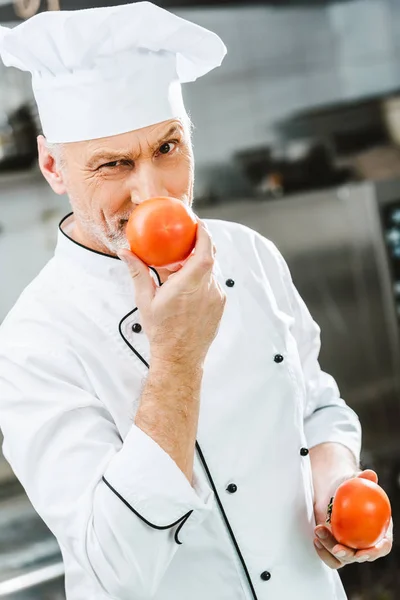 Chef masculino em uniforme e chapéu segurando tomates na cozinha do restaurante — Fotografia de Stock