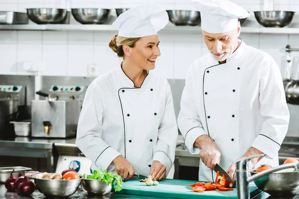 Chef di sesso femminile e maschile in ingredienti di taglio uniformi durante la cottura in cucina ristorante — Foto stock