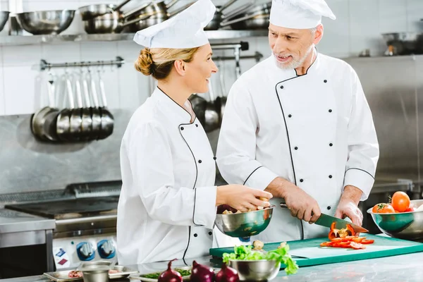 Chef di sesso femminile e maschile in ingredienti di taglio uniformi durante la cottura in cucina ristorante — Foto stock