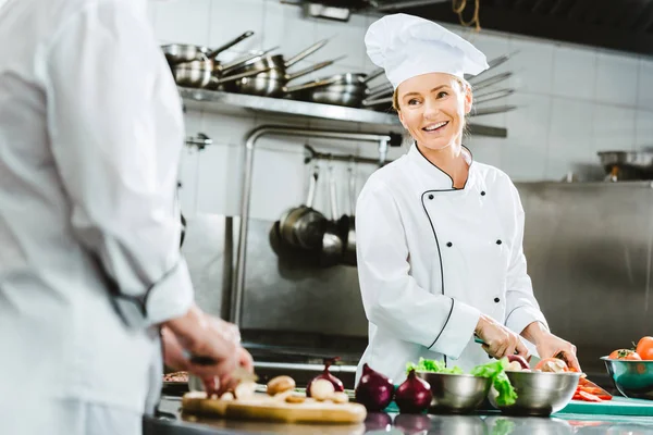 Beautiful female chef in uniform smiling while cooking in restaurant kitchen — Stock Photo