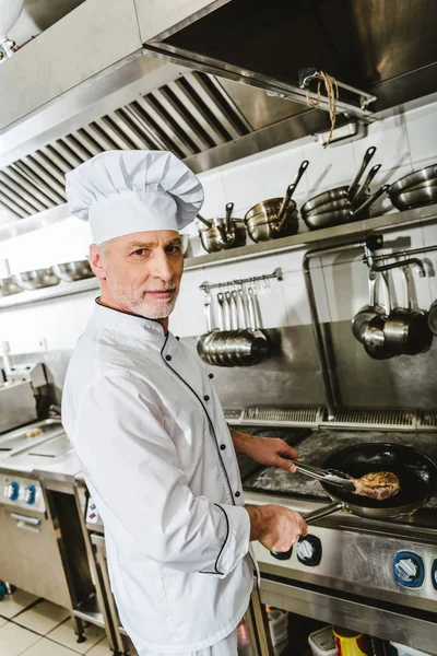 Male chef in uniform cooking meat in restaurant kitchen — Stock Photo