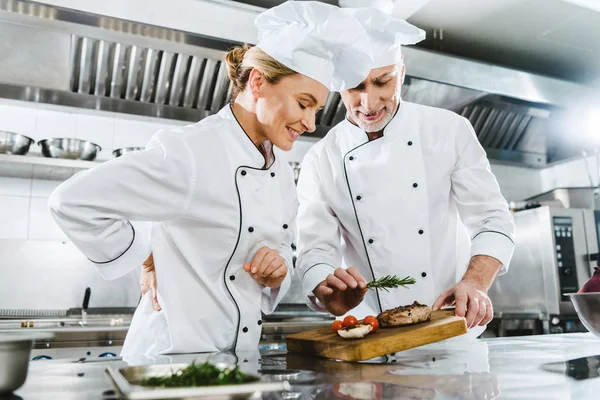 Chefs féminins et masculins en uniforme avec steak de viande sur planche en bois dans la cuisine du restaurant — Photo de stock