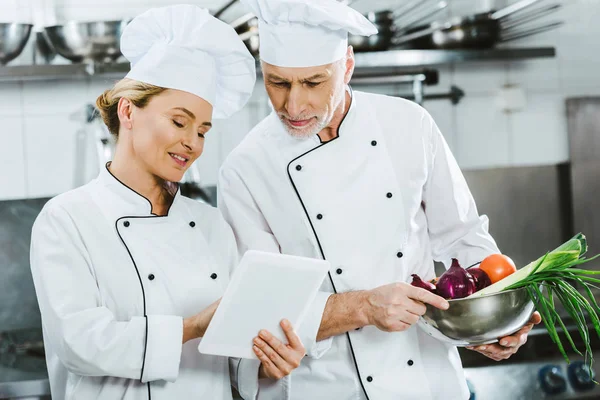 Female and male chefs in iniforms using digital tablet during cooking in restaurant kitchen — Stock Photo