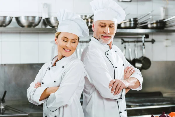 Smiling chefs in uniform with arms crossed at restaurant kitchen — Stock Photo