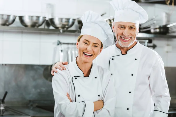 Femmes et hommes chefs en uniforme regardant la caméra et riant à la cuisine du restaurant — Photo de stock