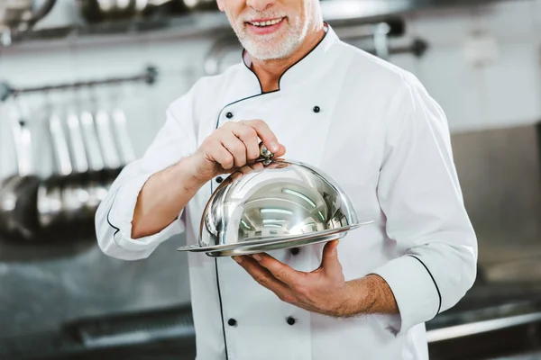 Vista cortada do chef masculino em bandeja de serviço uniforme segurando com cúpula na cozinha do restaurante — Fotografia de Stock