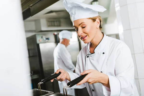 Bella chef donna in uniforme con friggitrice durante la cottura in cucina ristorante — Foto stock